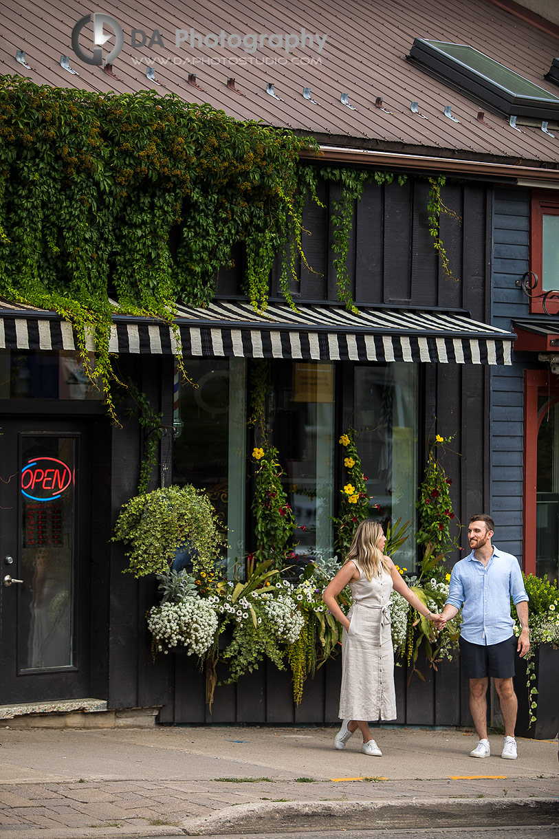 Engagement couple walking by storefront in the Village of Elora