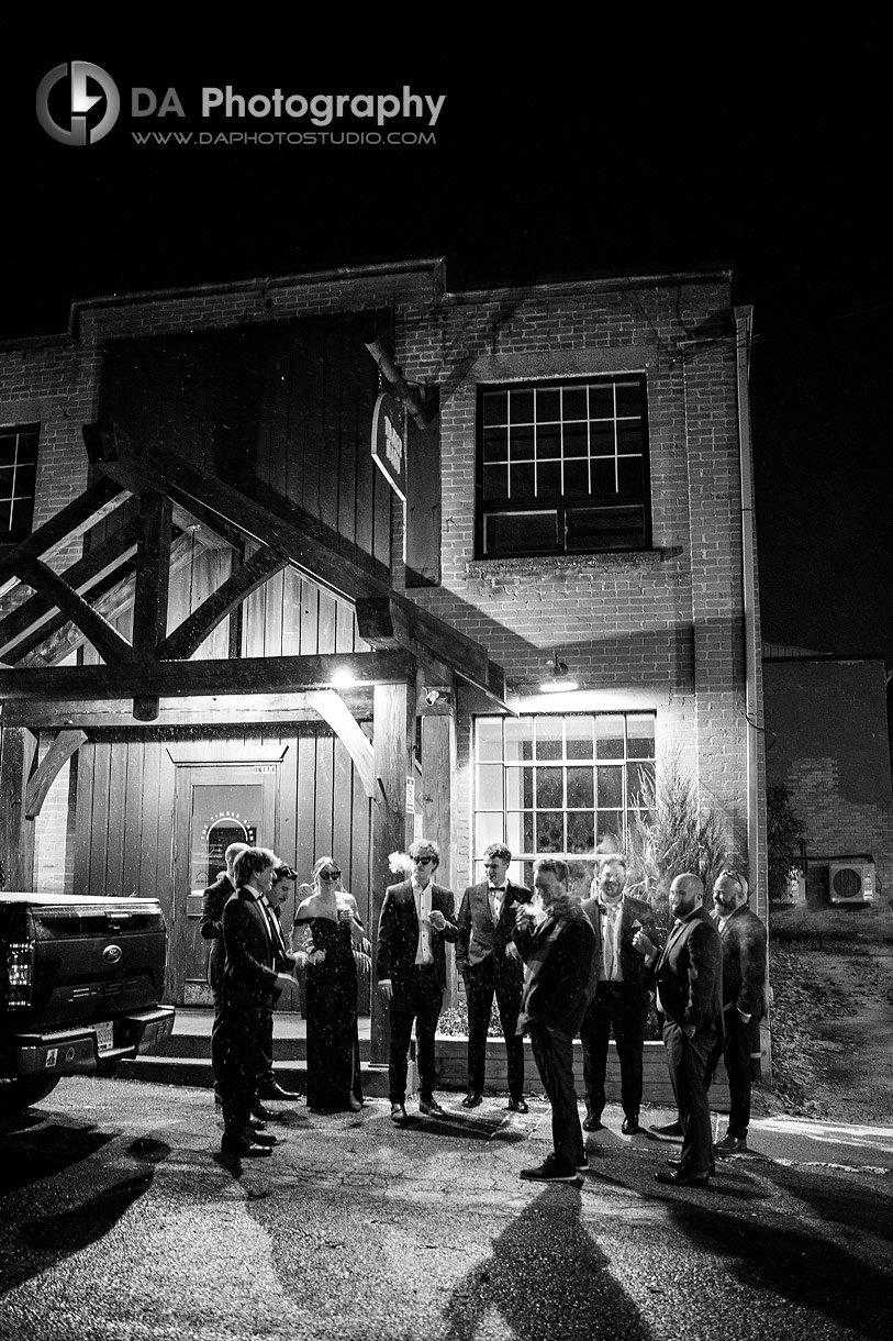 Photo of a Bridal party smoke cigars in front of Timber Barn