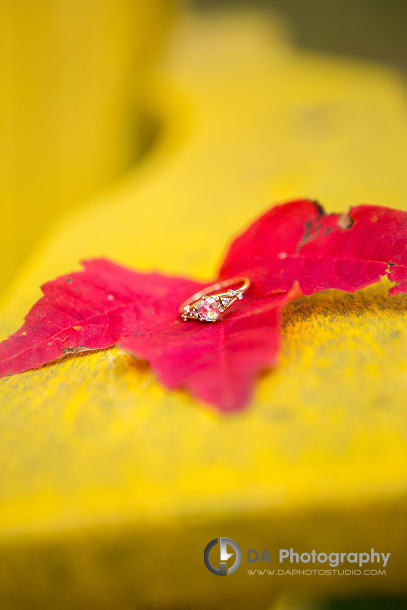 Close up Photo of an engagement ring placed on red maple leaf resting on yellow Muskoka chair