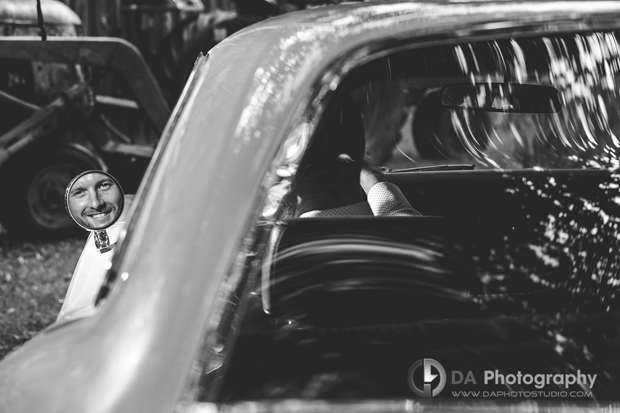 Photo of a reflection in the side mirror of a Groom in his vintage car