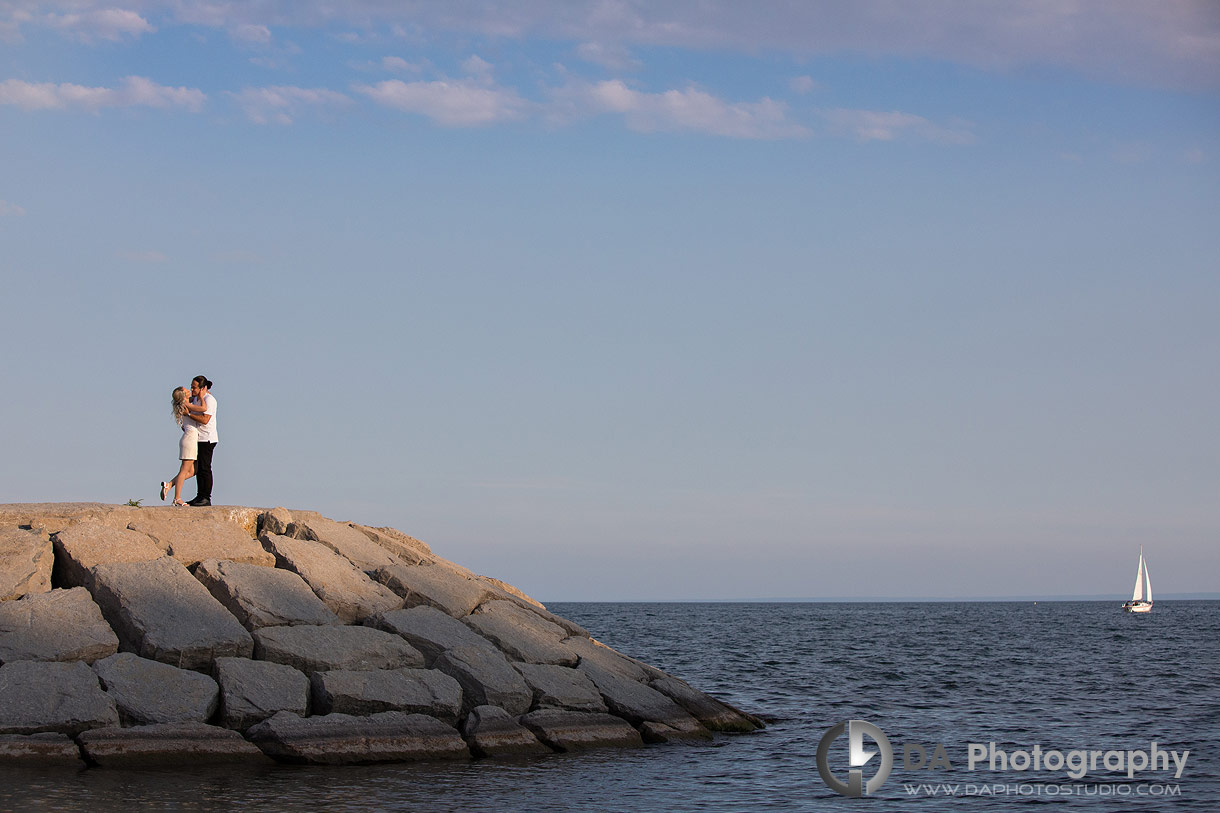 Couple standing near lakefront rocks during their waterfront engagement photos in Oakville